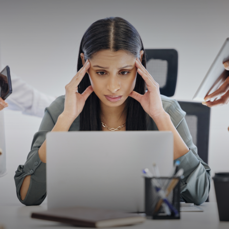 Frau sitzt gestresst am Schreibtisch vor einem Laptop. Von linkes und rechts ragen Hände herein.